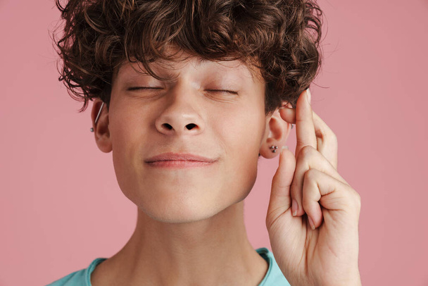 Smiling young man showing crossed fingers gesture on pink background. - Foto, afbeelding