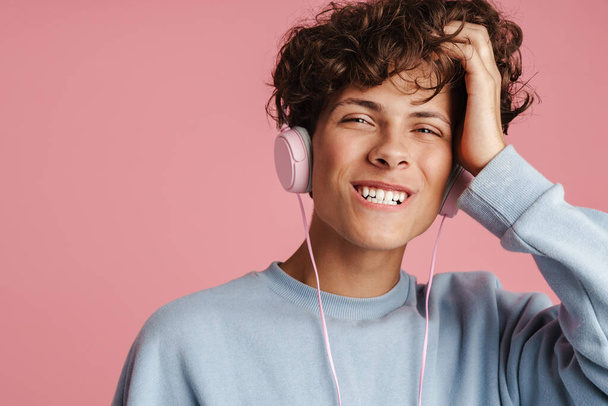 Primer plano de un joven y atractivo adolescente escuchando música con sus auriculares aislados sobre fondo rosa - Foto, Imagen
