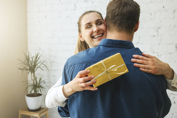 donna grata con scatola regalo che abbraccia marito a casa. sorpresa di compleanno o anniversario - Foto, immagini