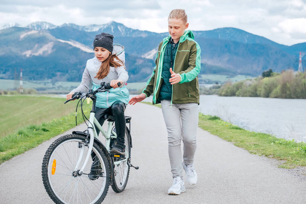  Brother carefully following his sister helping her and teaching doing first steps in bicycle riding. Happy outdoor childhood concept image. - Fotoğraf, Görsel