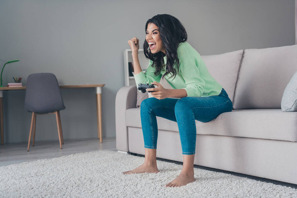 Full body photo of excited crazy dark skin woman sit couch play game hold joystick winner indoors inside house - Zdjęcie, obraz