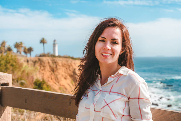 Приваблива жінка в білій сорочці йде вздовж берега з видом на маяк Пойнт Вісенте в Лос-Анджелесі. - Фото, зображення