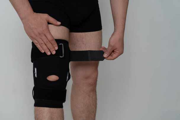 Leg support. A man adjusts a black orthosis on his leg. Copspace. - Фото, зображення