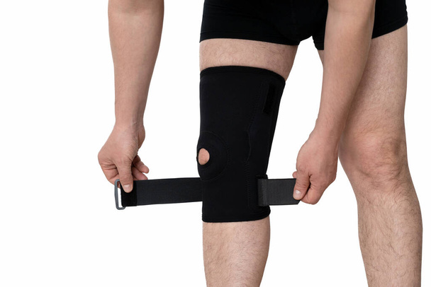 Orthosis on the male leg. A man fixes a black orthosis on his leg. Isolated on white background. - Valokuva, kuva