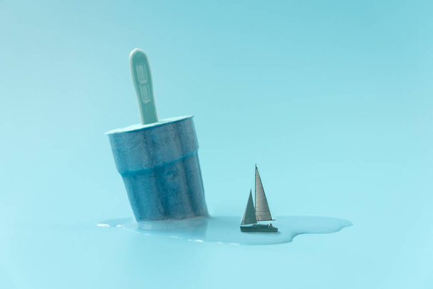 Ship sailing on melted ice cream on blue background.  Creative summer vacation concept - Foto, immagini