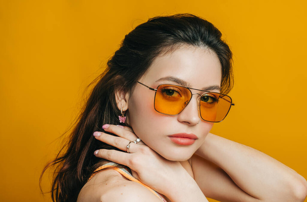 Portrait of attractive stylish woman in sunglasses with long brunette hair isolated on yellow background in studio. - Foto, Imagem