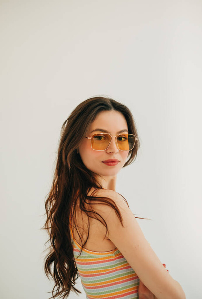 Portrait of attractive stylish woman in sunglasses with long brunette hair in studio. - Фото, изображение