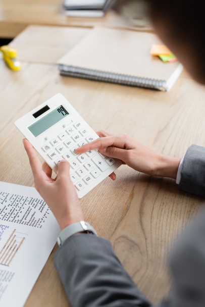 Обрізаний вид бізнес-леді, використовуючи калькулятор біля документа і розмитий блокнот
  - Фото, зображення