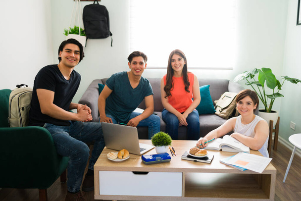 Oturma odasındaki kanepede ödev yaparken gülümseyen ve evde takılan bir grup üniversite öğrencisinin portresi.  - Fotoğraf, Görsel