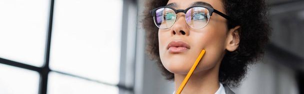 Low angle view of african american businesswoman with pencil looking away, banner  - Foto, imagen