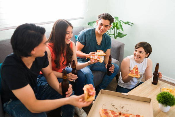 Amigos de la universidad bromeando y riendo juntos durante una pequeña fiesta en casa con pizza y cerveza - Foto, imagen