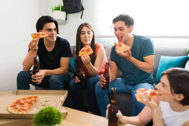 Sokszínű baráti társaság, akik jól érzik magukat, miközben a nappaliban lógnak. Egyetemisták együtt vacsoráznak sörrel. - Fotó, kép