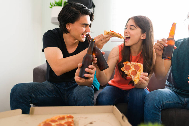 Funny boyfriend laughing and joking with his girlfriend while hanging out with friends. College man offering pizza to her female friend - Photo, Image
