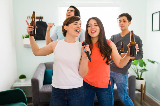 Красивые женщины лучшие друзья поют песню караоке вместе с помощью микрофона, тусуясь со своими парнями дома - Фото, изображение