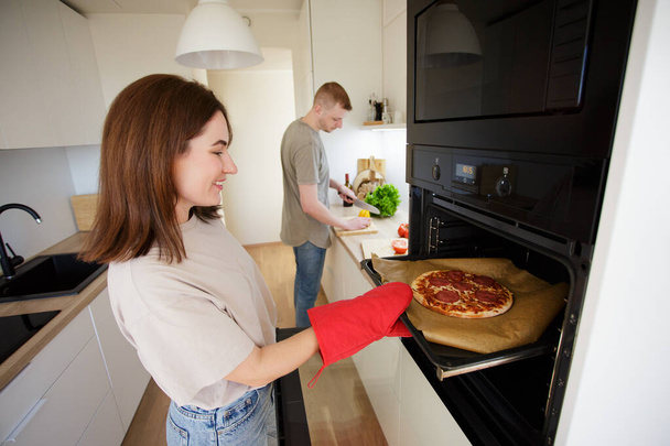 szczęśliwa młoda para robi pizzę w nowoczesnej kuchni w domu - Zdjęcie, obraz