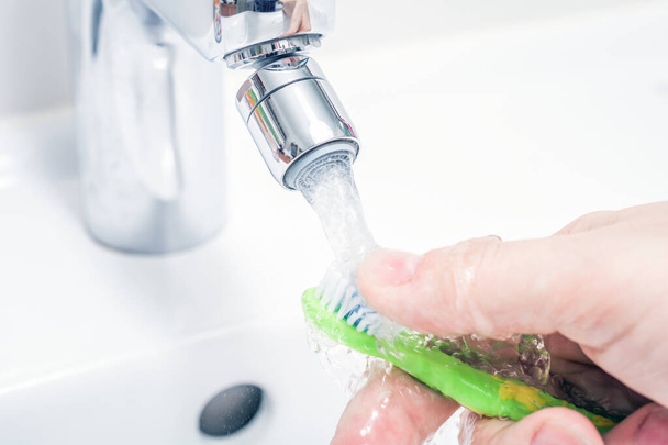 Cleaning A Toothbrush Under Pouring Water At Bathroom Sink - Foto, Imagen
