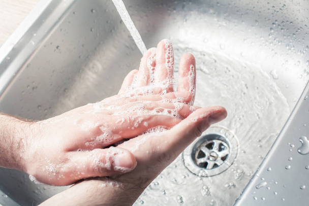 Egy férfi szappanozza a kezét, miközben vizet önt a konyhai mosogatóba. - Fotó, kép