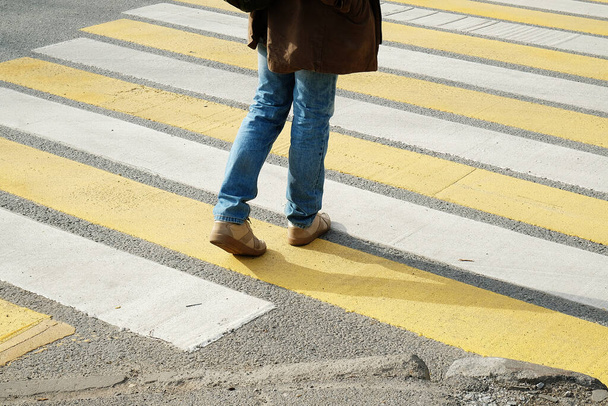 Человек переходит улицу по белым и желтым полосам пешеходного перехода - Фото, изображение