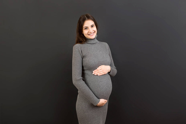 Счастливая беременная женщина трогает живот на цветном фоне. Будущая мать носит белое нижнее белье. Я жду ребенка. Копирование пространства. - Фото, изображение