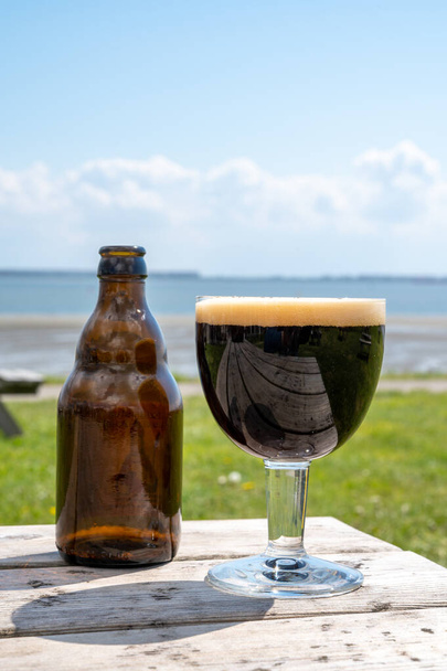 Bicchiere di birra belga scuro forte servita sulla terrazza all'aperto soleggiata con prato di erba verde sullo sfondo - Foto, immagini