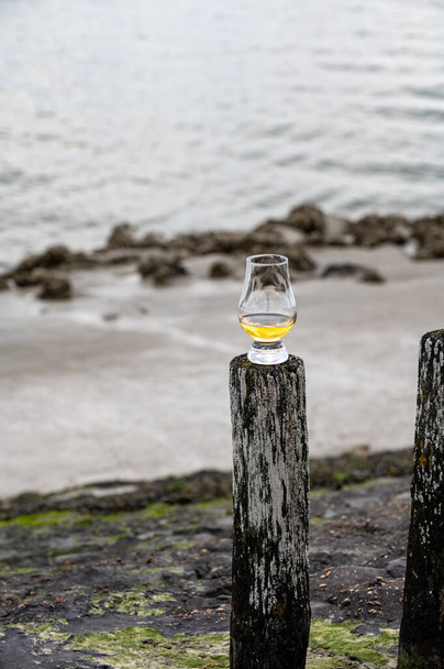 Proeverij van dram single malt whisky aan zee in Schotland, oude houten palen met whiskyglas - Foto, afbeelding