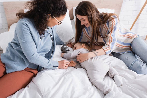 high angle view of happy interracial women looking at infant boy lying on bed  - Photo, image