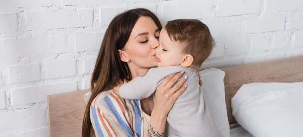 mère tatouée embrasser bébé garçon dans la barboteuse, bannière - Photo, image
