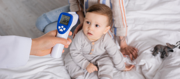 лікар вивчає немовля з безконтактним термометром біля матері, банер
 - Фото, зображення