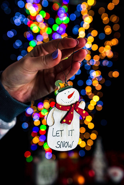 Holding Christmas snowman decoration isolated on background with blurred lights. December season, Christmas composition. - Fotografie, Obrázek