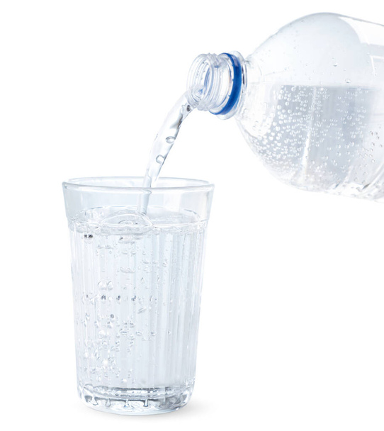 A víz egy üvegből egy közeli pohárba ömlik, fehér háttérrel. Elszigetelt - Fotó, kép