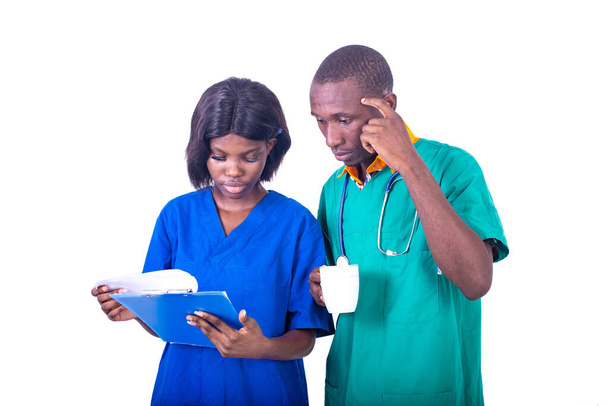 young male doctor holding a cup of coffee and explaining notes on clipboard to nurse at hospital. - Photo, Image