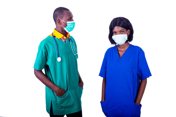 een groep artsen in uniform staan op witte achtergrond dragen maskers met handen in zakken - Foto, afbeelding