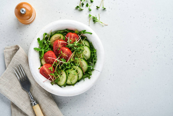 Fresh salad with tomato, cucumber, vegetables, microgreen radishes in white plate on grey stone background. View from above. Concept vegan and healthy eating. - Valokuva, kuva