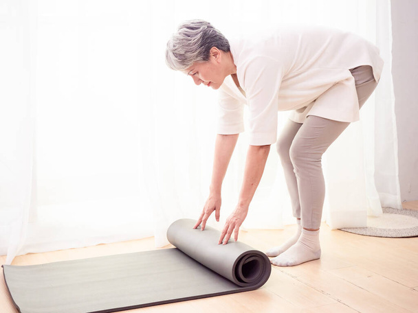 Senior asiatico donna esercizio a casa sanità holding yoga mat - Foto, immagini