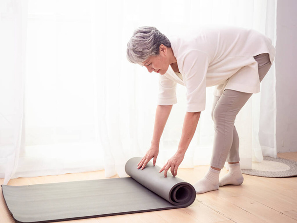 Senior asian woman exercise at home health care holding yoga mat - Foto, afbeelding