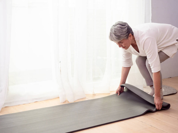Senior asiatisch frau exercise at home health care holding yoga matte - Foto, Bild