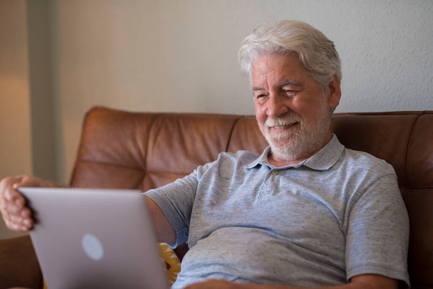 Счастливый пожилой человек в помещении, работающий за ноутбуком и улыбающийся, расслабленный пожилой мужчина, пользующийся компьютером или серфингом в Интернете, читающий новости онлайн - Фото, изображение
