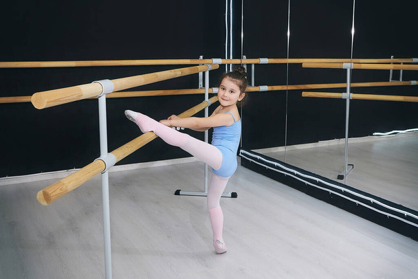 little girl does exercises in the hall of the choreographic school with a ballet barre - Photo, image