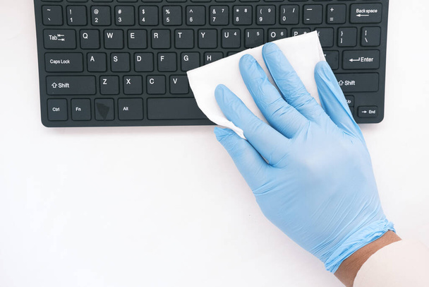 kéz kék gumikesztyűben és fehér szövet fertőtlenítő billentyűzet  - Fotó, kép
