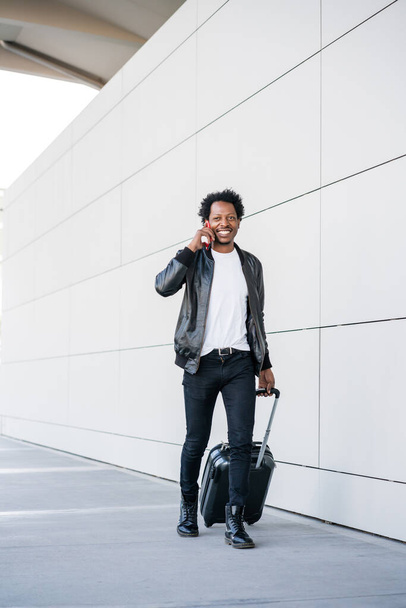 Tourist man talking on phone and carrying suitcase outdoors. - Valokuva, kuva