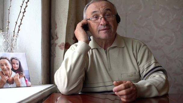 Mosolygó idős férfi visel fülhallgató integetni a kamera videohívás laptop, boldog idős férfi fülhallgató ülni kanapén otthon beszélgetés segítségével modern technológiák és vezeték nélküli kapcsolat - Fotó, kép