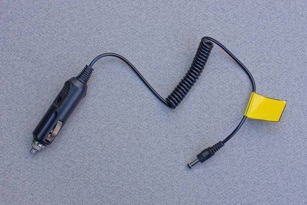 a black car charger with an electric wire and a plug lies on a gray table - Photo, Image