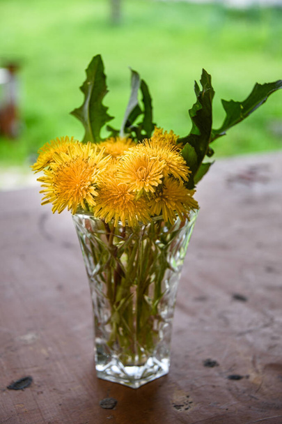 木製のテーブルの上にクリスタル花瓶に黄色のタンポポの花束。野の花の美しさ. - 写真・画像