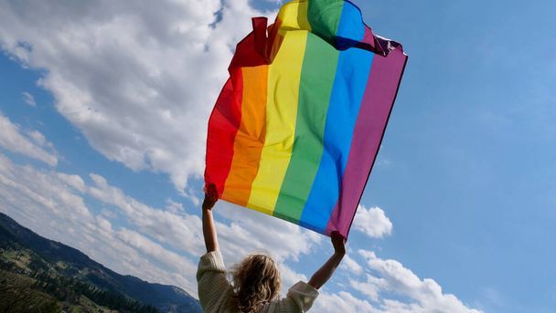 空にLGBTの旗を掲げる女性 - 写真・画像