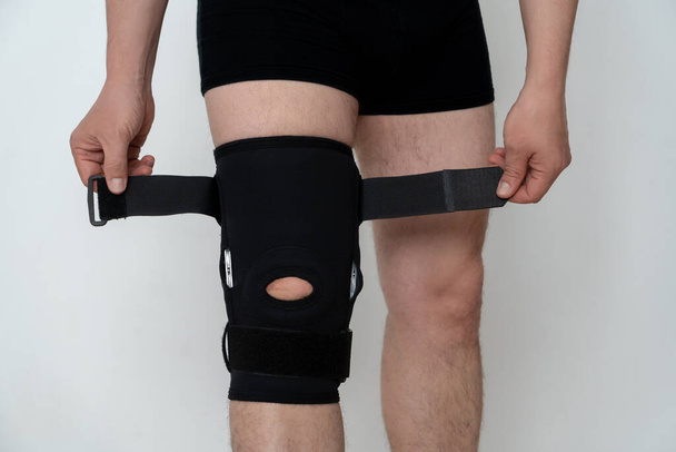 Leg support. A man adjusts a black orthosis on his leg. Copspace. - Fotó, kép