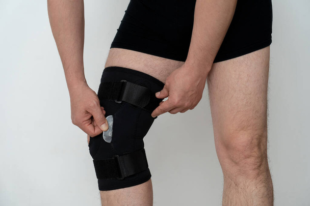 Leg support. A man adjusts a black orthosis on his leg. Copspace. - Photo, Image