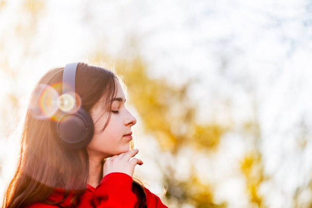 Glückliches Mädchen, das mit Kopfhörern in einem Park Musik hört. Teenagermädchen mit drahtlosen Kopfhörern. - Foto, Bild