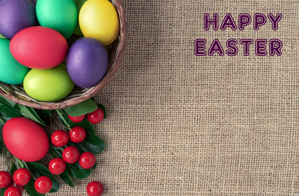 Huevos de Pascua en una canasta de mimbre, bayas rojas y la inscripción "Feliz Pascua". - Foto, Imagen