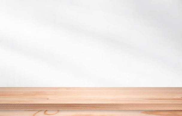 Long pine wooden table in front of wall with soft light. Empty desk, shelf or tabletop for template.  - Foto, Imagem