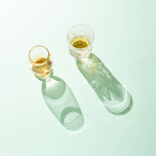 Δύο ρετρό ποτήρια με ποτά και τις μακριές σκιές τους σε ανοιχτό πράσινο φόντο. - Φωτογραφία, εικόνα